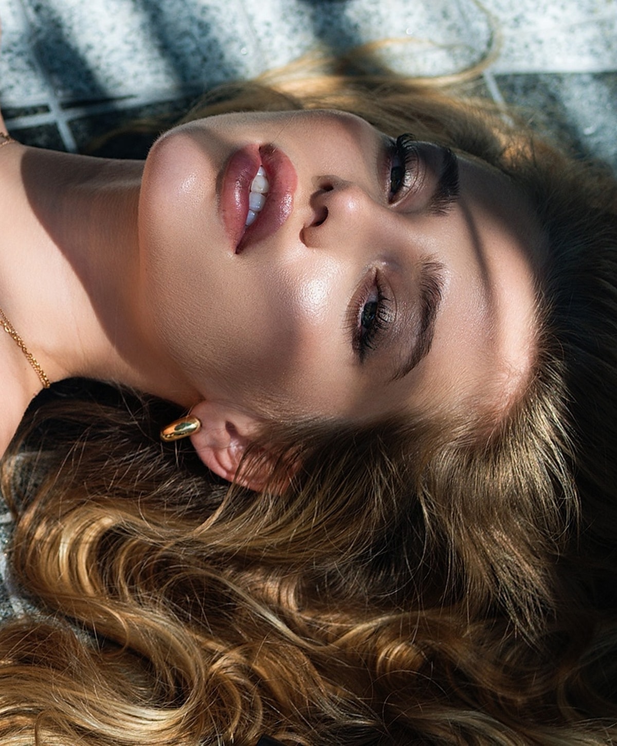 Woman with wavy hair lying on a textured surface.
